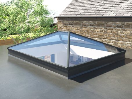 Glass skylight on a flat roof, surrounded by greenery and a stone wall.